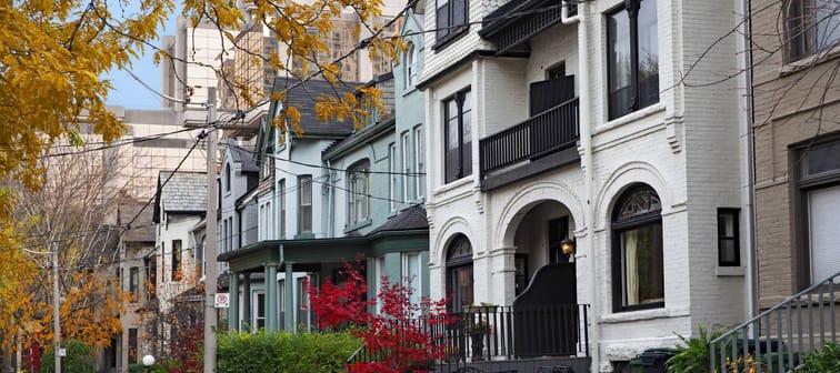 Street of historically designated old Victorian houses with gables and painted brick, downtown Toronto, with large office building in background