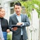 Asian young realtor showing photos of new house to young family on tablet pc while they walking along the street