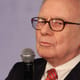 Warren Buffett holds a microphone and looks to the side of the camera with his eyes narrowed