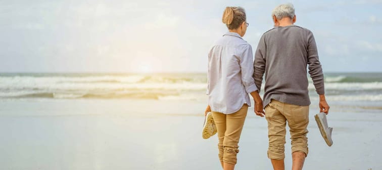 Senior couple walking on the beach holding hands at sunrise