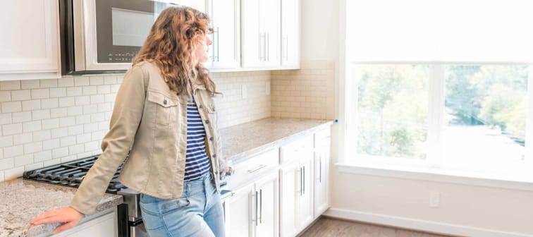 One young woman standing in kitchen in clean, modern, white home design before move-in