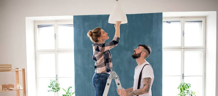 Mid adults couple changing light bulb indoors at home, relocation and diy concept.