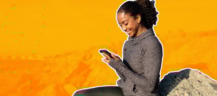 Woman on rocky beach smiling at phone