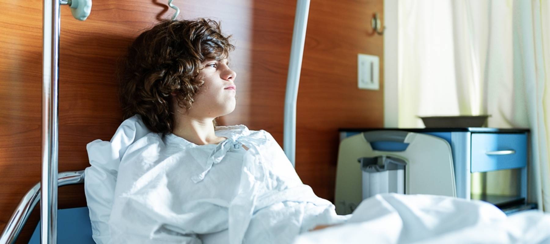 Young boy in a hospital bed looking sad and off to the side.