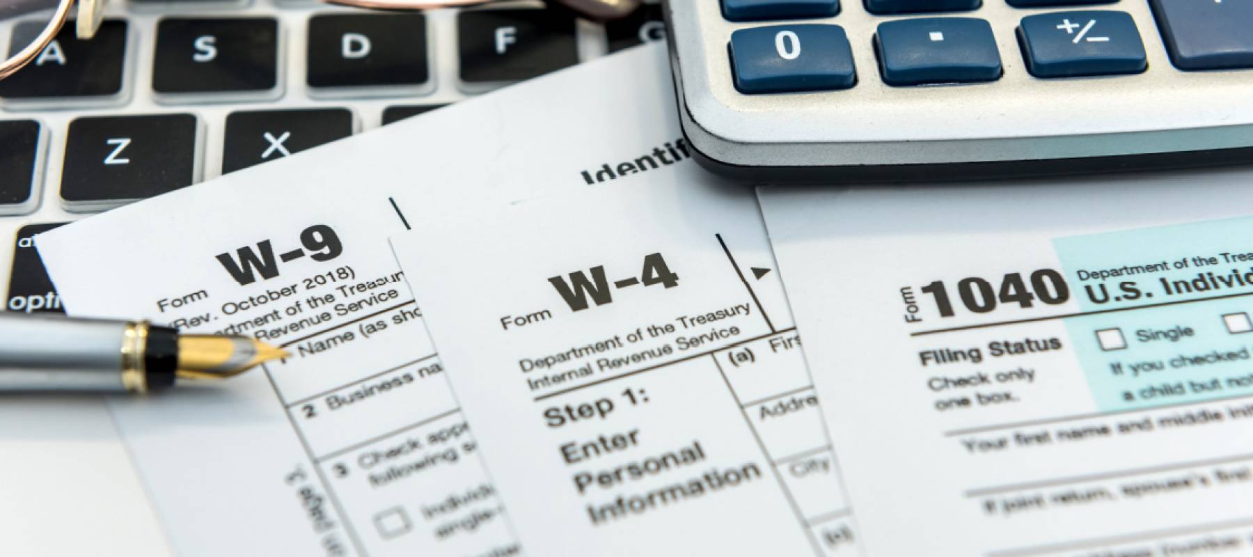 past tax return paperwork w9 w4 1040 with calculator laptop and glasses