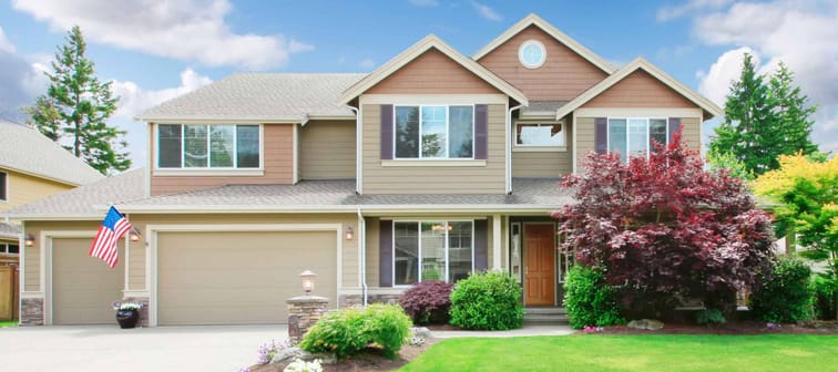Beige large luxury house with summer landscape with blue sky and American flag.