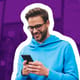 Happy young man sits on a bench outside, looking down at his phone.