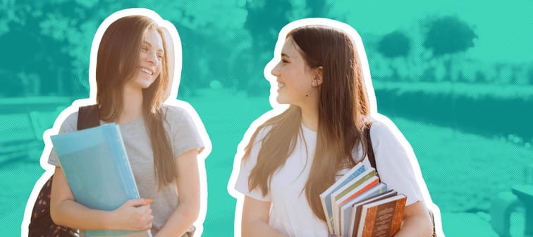 Two happy student girls walking and talking to each other on campus.