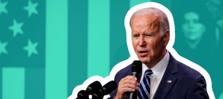 President Joe Biden holds a microphone and makes a pained face while talking.