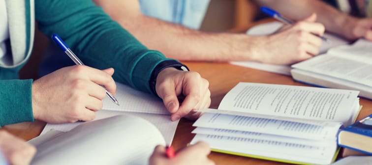close up of students hands with books or textbooks writing to notebooks