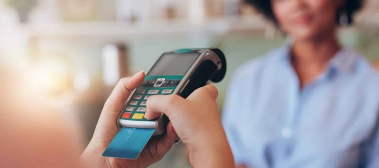 Young woman paying by credit card at juice bar. Focus on woman hands entering security pin in credit card reader.