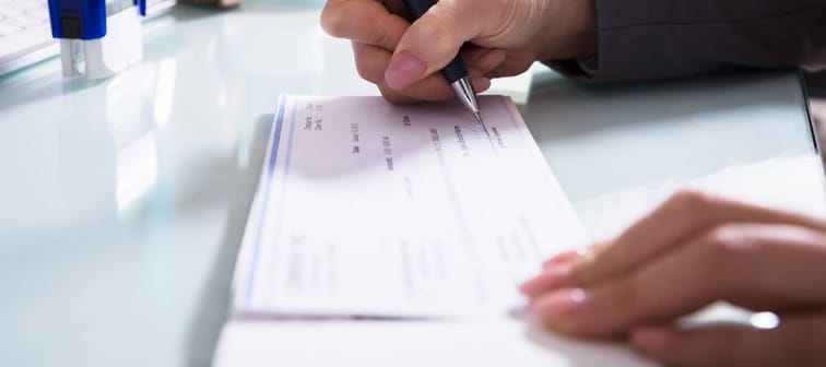 Close-up Of A Businessperson's Hand Signing Cheque With Pen In Office