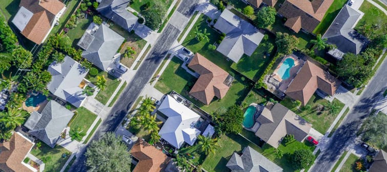 Aerial summer view of warm sunny neighborhood community roofs with diagonal streets and lots of houses with pools and palm trees.